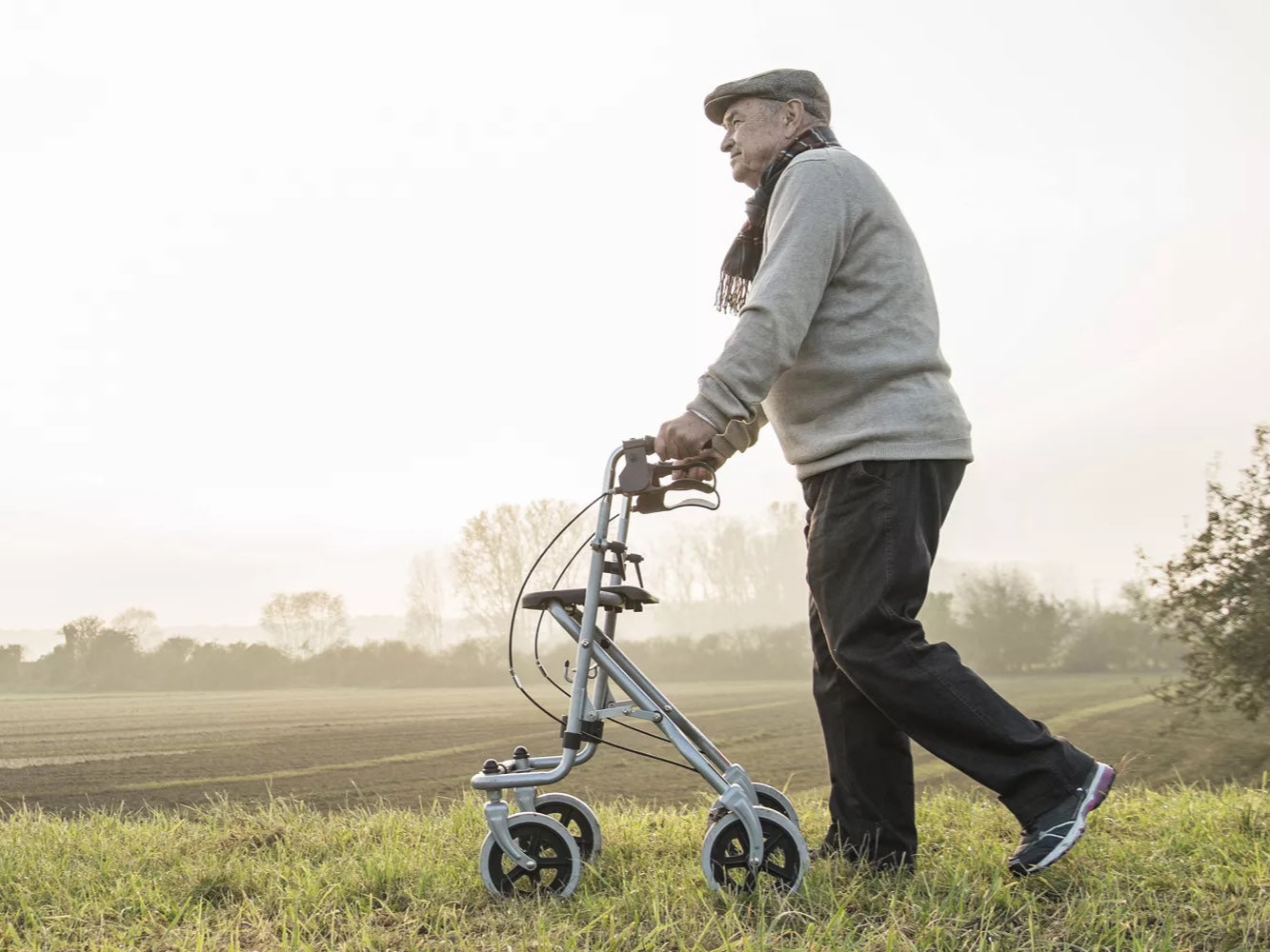 Older man walking with a rollator across a misty morning field — RIDE Cyclery services hand-brake walkers for our Encinitas neighbors
